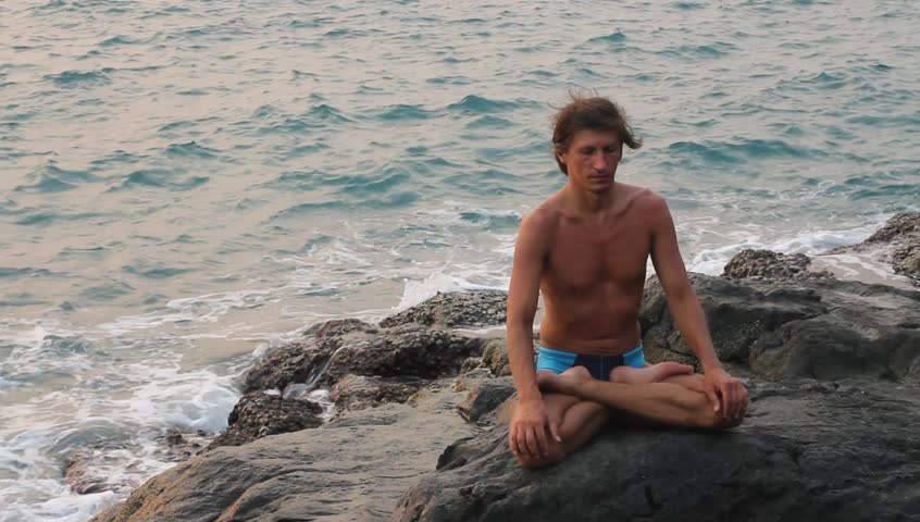 Man doing yoga exercise on the deserted wild stone sea beach (HD)