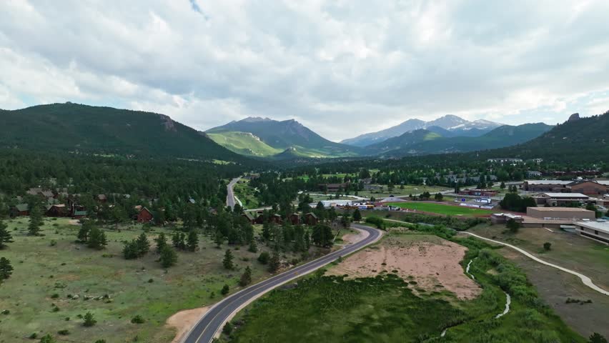 Drone ascends along winding road into Estes Park Colorado in valley of Rocky Mountains