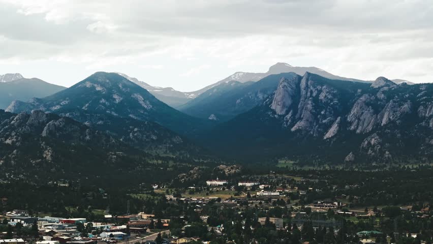 Light cast over rocky mountains as drone descends on Estes Park on cloudy day