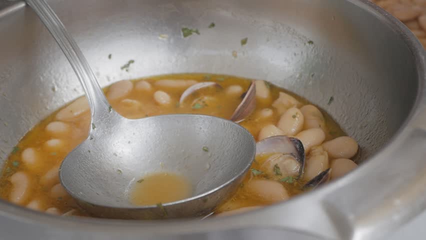 Someone scoops white or haricot beans stew from the bottom of the pot at one of the finest restaurant in Spain. Traditional dish Fabes con Almejas, Beans with clams.