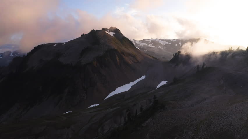 Golden yellow light in sky with clouds as mountain peaks with snow darkens at sunset