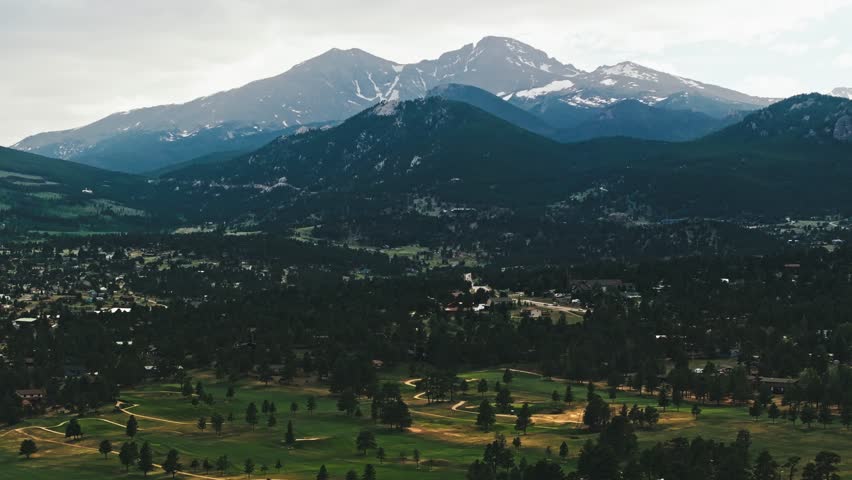 Pan right over municipal parks in Estes Park Colorado with tall ridges of Rocky Mountains in distance