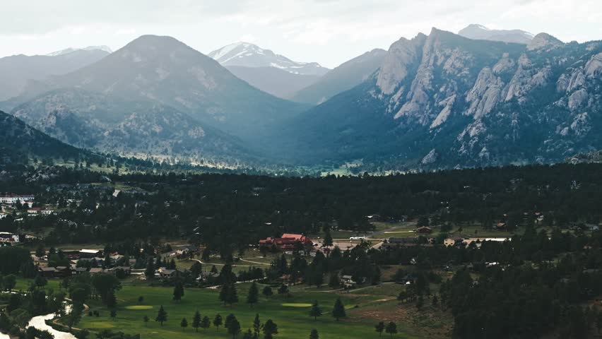 Drone pan right above parks and alpine forested areas of Estes Park Colorado with shining light across mountains