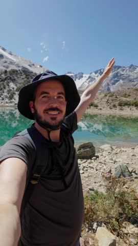 Vertical POV video selfie of young happy tourist man in front of Humantay lake in Peru, on Salcantay mountain in the Andes, South America. Adventure and travel concept.