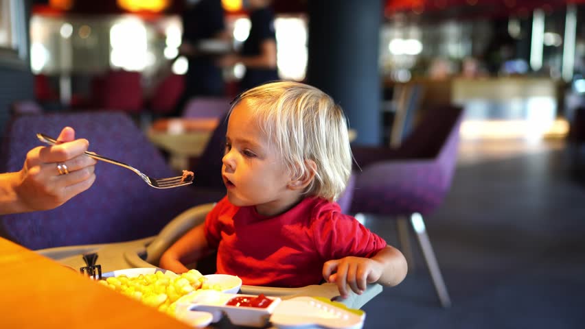 Mom feeds a little girl with pieces of meat, and she spits them out