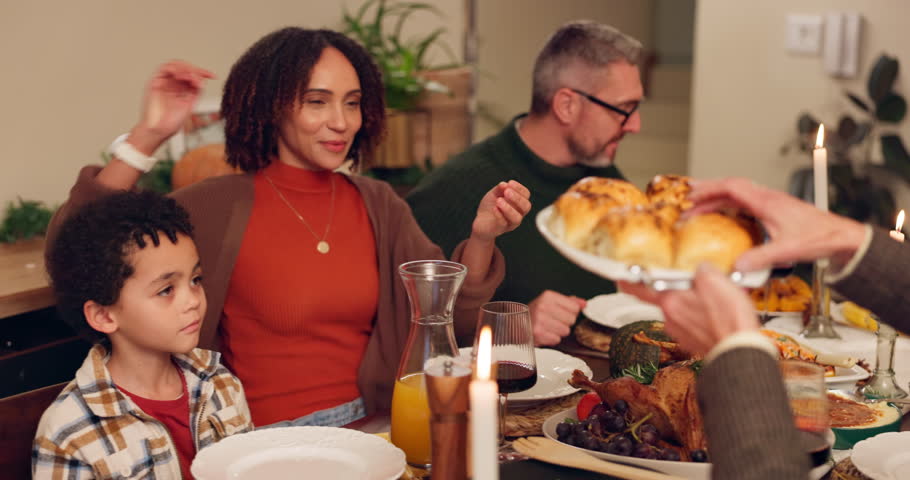 Food, happy family and eating dinner for thanksgiving celebration or gratitude in home at night. Child, mom and dad share meal in plate or serving bread buns and interracial people bonding together