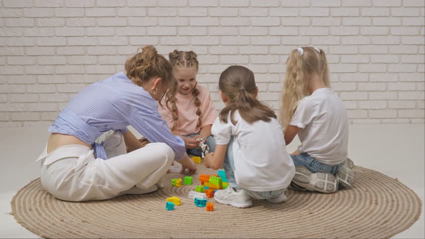 Young woman teacher and group of toddlers children sitting on the floor and playing toy constructor in developmental classes. Children education concept.