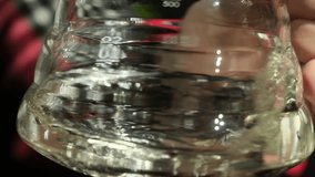 Glass beaker keeps clear liquid with swirling clean substance. Round vessel contains transparent fluid of small amount of water slow motion - Powered by Shutterstock - Get 15% off with code: PIKWIZARD15