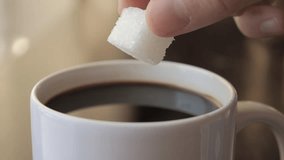Slow Motion Hand Dropping Sugar Cube Into Black Coffee. Sugar Falling Down Into Coffee Cup. Coffee Caffeine Addiction Junk Food. Concept of Unhealthy Eating, Diabetes, Obesity, Heart Disease.  - Powered by Shutterstock - Get 15% off with code: PIKWIZARD15