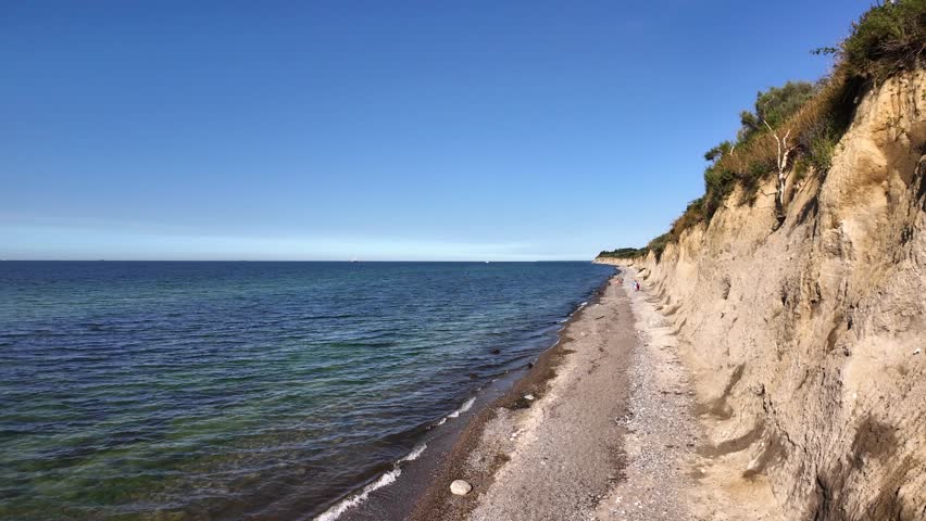 Unrecognisable fearless people walking on a dangerous narrow Baltic Sea beach next to a landslip area. Erosion of the sand cliffs is a huge problem along the coast. Sunny summer day in North Germany.