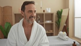 Mature man in a spa setting wearing a white bathrobe, surrounded by wellness interior with plants, rolled towels, and minimalist decor creating a relaxing atmosphere - Powered by Shutterstock - Get 15% off with code: PIKWIZARD15