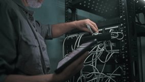 Male specialist inserts cable into server rack. Network administrator works in server room using tablet computer. Maintenance of computer networks or web servers. Data storage center. Slow motion. - Powered by Shutterstock - Get 15% off with code: PIKWIZARD15