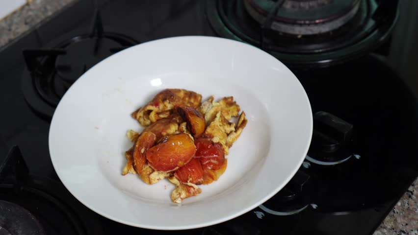Woman putting frying eggs with tomatoes from hot oiling  pan into plate in kitchen at home. Thai style.