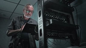 Mature technician works in server room. System administrator inserts cable into server rack and configures operating systems using tablet computer. Local area network maintenance. Data storage center. - Powered by Shutterstock - Get 15% off with code: PIKWIZARD15