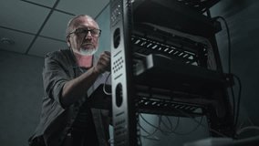 Mature technician works in server room. System administrator inserts cable into server rack and configures operating systems using tablet computer. Local area network maintenance. Data storage center. - Powered by Shutterstock - Get 15% off with code: PIKWIZARD15