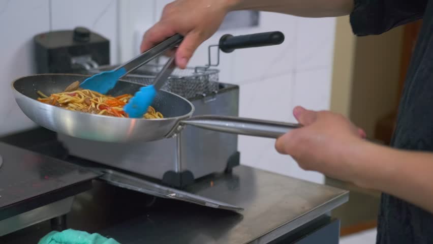Cooking white soba noodles with beef and vegetables in a frying pan to be sent to the client in a paper wok box.