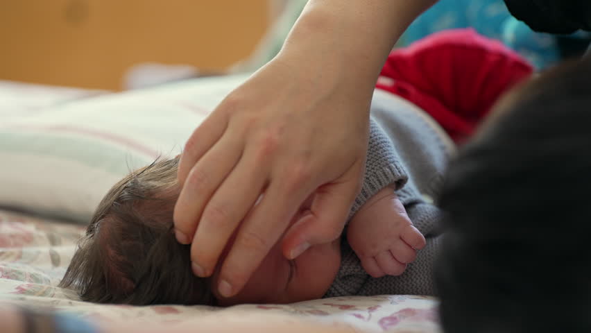Close-up of a sleeping baby in a cozy bed, with a gentle hand caressing the infant's head, capturing a moment of peace, comfort, and security in a warm and loving home