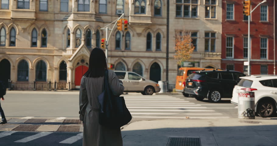 Medium shot of beautiful busy brunette walking in urban street of New York City with a busy traffic on bright sunny day