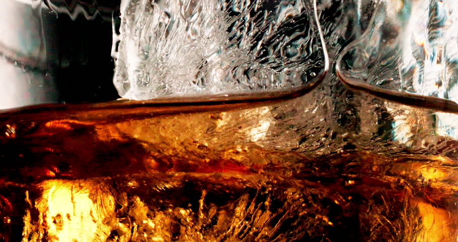 Glass, ice and pour liquid in studio for enjoyment, closeup and cold beverage. Frozen cube, tumbler and whiskey flow on black background with liquor, brandy and aesthetic for testing in distillery