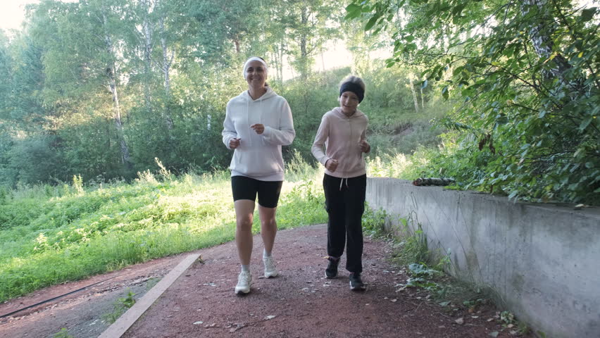 Cheerful mother and her young daughter enjoy a refreshing run together in a serene park early in the morning, surrounded by lush greenery, Healthy lifestyle concept