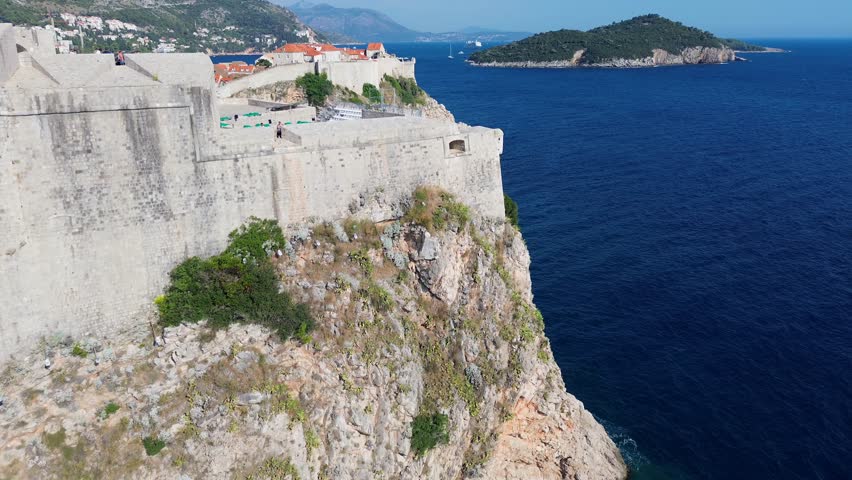 Aerial drone film of the historic, ancient walled city of Dubrovnik in Croatia on the Adriatic Sea. Summer colourful city view with defence wall, narrow illuminated streets tiled roofs and fort church