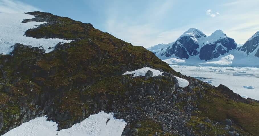 Amazing Antarctica mountains winter landscape. Green rock hill, frozen ocean, ice snow covered island glacier in background. Antarctic wild nature travel exploration. Tourism expedition to South Pole