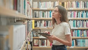 Caucasian female wearing glasses with a tablet marking books in the library, working on a science project, doing tutor homework. Book selection, teacher prep, higher education, student e-learning - Powered by Shutterstock - Get 15% off with code: PIKWIZARD15