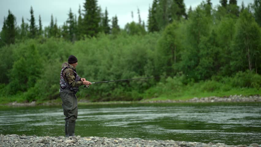 A fisherman stands on the river bank and catches fish with a spinning rod near 