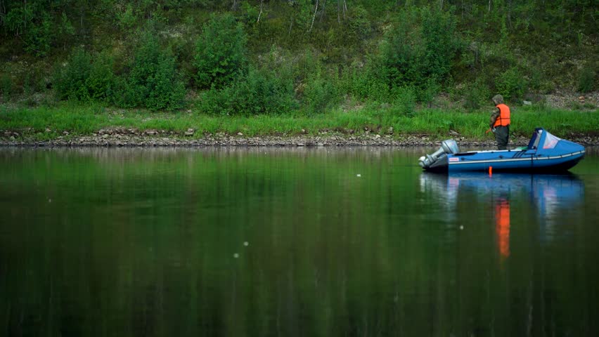 A fisherman floats on an inflatable boat on a lake and fishes