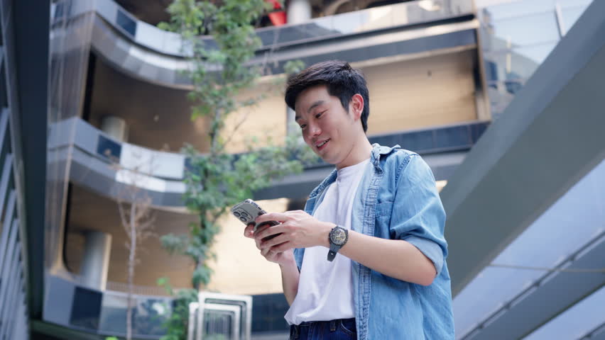 Handsome Asian student using smartphone. A young man standing outdoor happy smiling with holding mobile phone