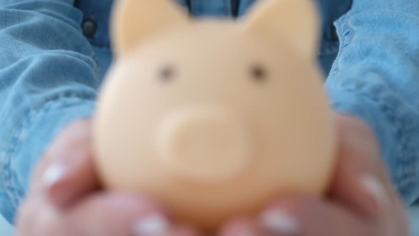Female hands holding blue piggy bank on white table. Saving money, wealth and financial planning concept