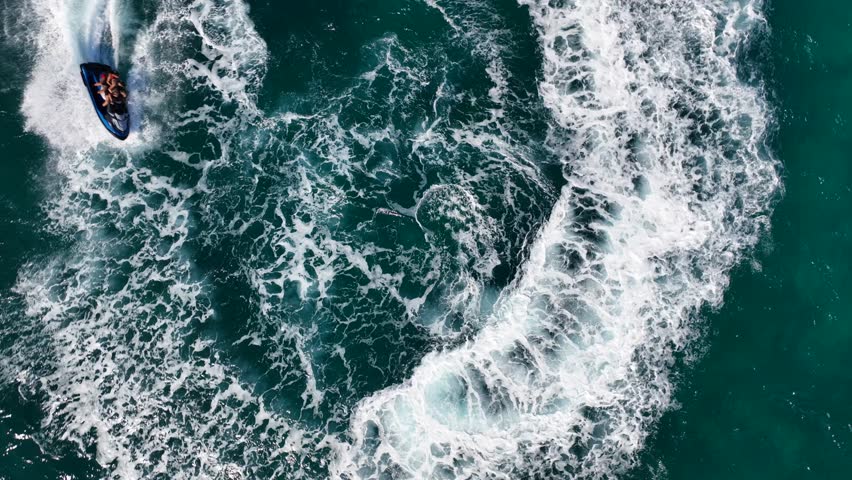 Aerial drone tracking video of jet ski watercraft performing extreme manoeuvres showing off in high speed operated by stuntman in deep blue sea