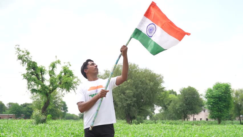 Indian young man wearing national flag logo design printed t shirt and holding, waving or running with Tricolour with greenery in the background, celebrating Independence or Republic day