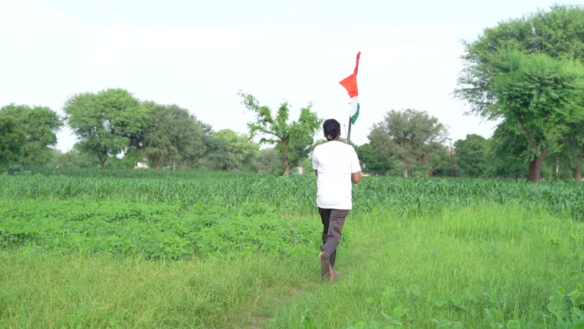 Indian village kids wearing national flag logo design printed t shirt and holding, waving or running with Tricolour with greenery in the background, celebrating Independence or Republic day