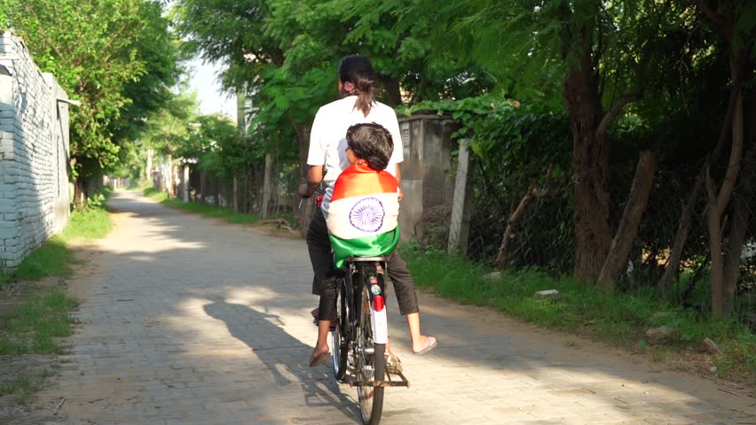 Indian village kids wearing national flag logo design printed t shirt and holding, waving or running with Tricolour with greenery in the background, celebrating Independence or Republic day