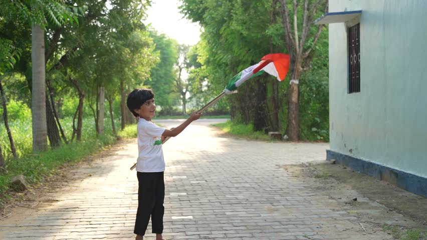 Indian village kids wearing national flag logo design printed t shirt and holding, waving or running with Tricolour with greenery in the background, celebrating Independence or Republic day