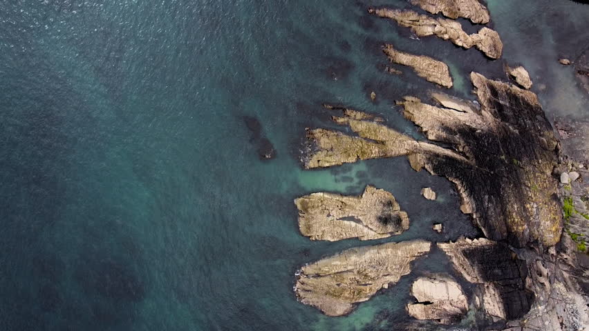 Clear waters reveal rocks along a rugged coastline during low tide, showcasing the natural beauty of the shoreline.
