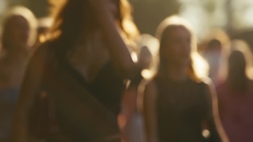 Bokeh blurred people crowd walking busy street slow motion shot, city life, lot of unrecognizable pedestrians, brightly lit crowded sidewalk, urban rush hour summer day. Sun beams warm orange sunlight