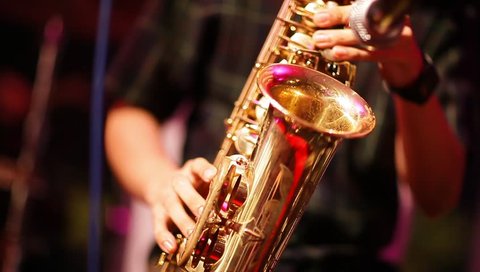 Musician is playing on saxophone in concert. Close-up on fingers pressing the keys of the instrument