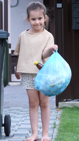 vertical video portrait of a little girl with a garbage bag near a trash can