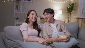 Asian young loving couple watch movie together in living room at home. Attractive romantic new marriage man and woman sitting on sofa, looking at TV show and having fun laughing together in house. - Powered by Shutterstock - Get 15% off with code: PIKWIZARD15