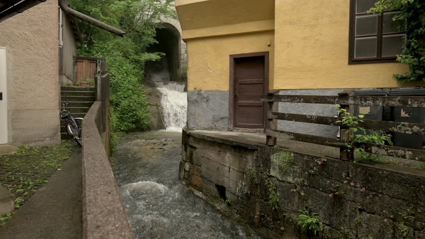 A narrow alleyway in Hallstatt, Austria, featuring a flowing stream and rustic buildings, creating a quaint and charming scene.