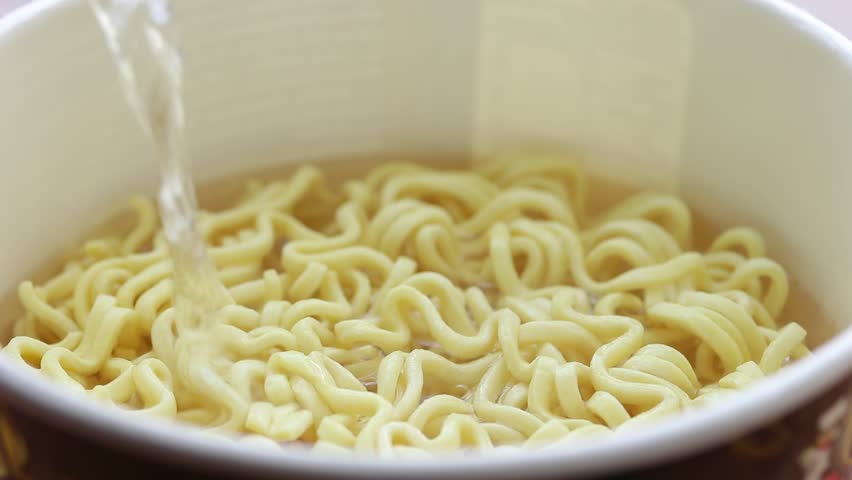 Pouring hot water into instant noodles cup. Close-up shot