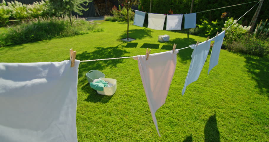Clothes hang on a line in a sunlit backyard, casting shadows on the green lawn below.