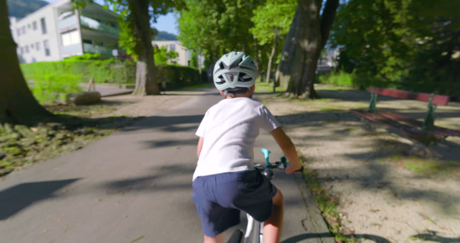 Young boy cycling in an urban setting, wearing a helmet for protection, sun shining brightly, showcasing outdoor activity