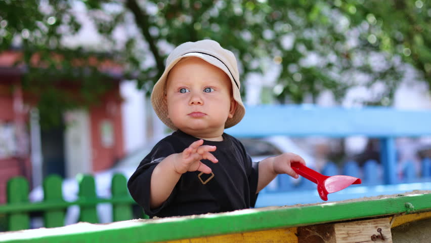 A cute blond boy, 1 year old, is playing on the street. A walk with a baby. Child development. A boy in a t-shirt on a sunny day. Vertical video.