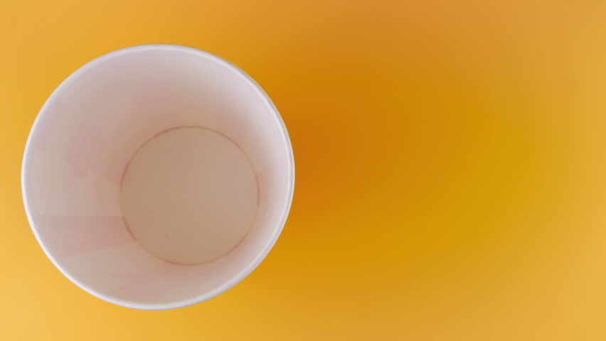 Popcorn grains falling into red and white striped bucket isolated on peach background. Movie snack food, fast food cafe sweet snack. Top view. Slow motion.