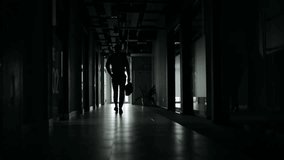 Silhouette of a businessman walking alone down a dark office hallway towards a bright window, exiting the building. - Powered by Shutterstock - Get 15% off with code: PIKWIZARD15