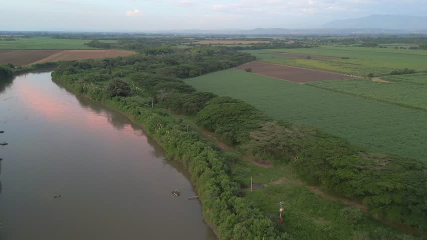 Aerial View of Cauca River At Sunset with Water Reflection. Sugar Cane Crops. Pull Back Shot. Valle del Cauca. Colombia