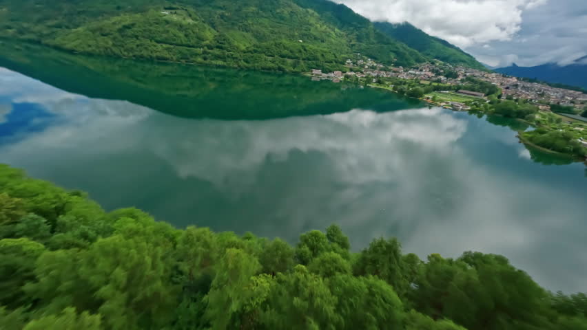 Serene aerial view of Lago di Levico with lush green hills and town reflections on a cloudy day
